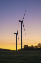 Two wind turbines rise at dusk. The sky shows a soft color gradient, in keeping with the peaceful