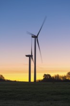 Wind turbines in motion in front of a colorful sunset. The silhouettes of the turbines dominate the