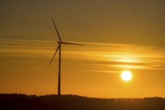 A single wind turbine in front of an intense orange sunset. The sky glows with bright colors,