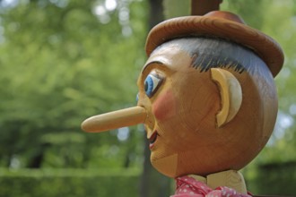 Pinocchio sculpture with long nose and blue eyes as a wooden figure, symbol of lies, long, wooden