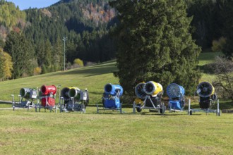 Different snow cannons on an extensive meadow in front of a forest in autumn, Schwangau near