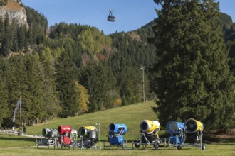 Snow cannons in a meadow surrounded by mountains and autumn forests, Tegelbergbahn cabin in the
