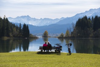 Two people sitting on a bench enjoying the view of the peaceful Forggensee and the majestic