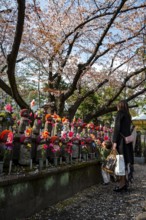 Mother and child in front of Jizo statues with red crocheted caps, guardian deities for deceased