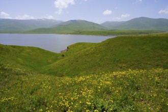 Green hills surround a calm lake under blue sky, spring-like atmosphere, Spandaryan Reservoir,