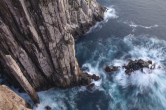 Long exposure at sunrise shows glowing dawn over the dramatic cliffs of Cape Hauy. Gentle waves hit