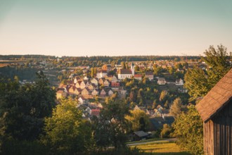 Evening in a hill village, centrally a church, surrounded by many houses and trees, Altensteig,