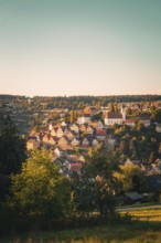 View of a village with church on a hill, warm sunlight shimmering through the trees, Altensteig,