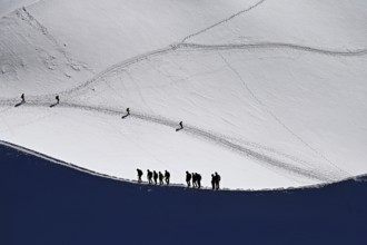 A group of mountaineers runs across a snow-covered mountain ridge, Aiguille du Midi,