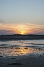 Sunset on a quiet beach with soft light on the waves, wet beach at low tide, dunes in the
