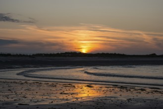 Sunset on a quiet beach with soft light on the waves, wet beach at low tide, dunes in the