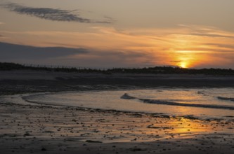 Sunset on a quiet beach with soft light on the waves, wet beach at low tide, dunes in the