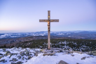 Christian cross on the peak of Mount Lusen with the view over the hills of the bavarian forest at