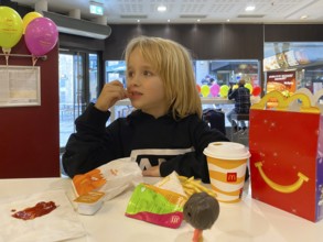Interior view, child, boy, 7 years, blonde, eating Happy Meal, children's menu, at McDonald's