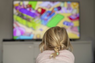 Child, girl, 4 years old, blonde, lying on sofa, watching TV, watching television, in front of
