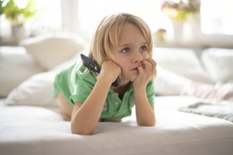 Child, boy, 7 years old, blonde, lying on sofa with remote control in hand, watching TV, watching