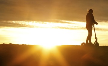 E-scooter drivers ride across a dike on the island of Fehmarn at sunset, 13.10.2025, Fehmarn,