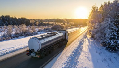 Petrol cargo truck lorry tanker driving on highway hauling oil products at sunrise, wide snowy