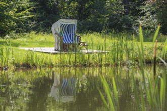 Single beach chair by a pond in a park, reflection, Westphalia, North Rhine-Westphalia, Germany