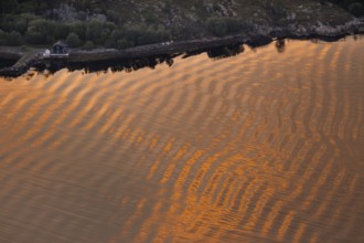 Warm sunlight reflects on gentle waves in a bay at sunset, forming a wave-like pattern, Otroya or
