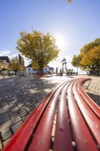 Red benches on a sunny town square surrounded by autumnal trees, Überlingen, Lake Constance,