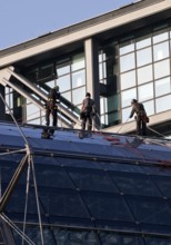 Three male glass cleaners abseiling down a glass roof of Berlin Central Station to clean windows,