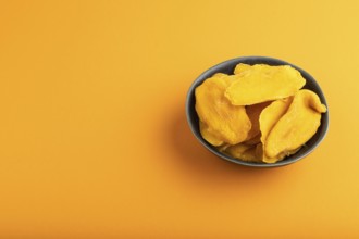 Dried Mango in blue ceramic bowl on orange pastel paper background. Side view, copy space. healthy