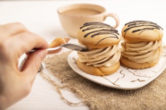 Caramel Cream Cakes with hand on white wooden background and linen textile, cup of coffee, side
