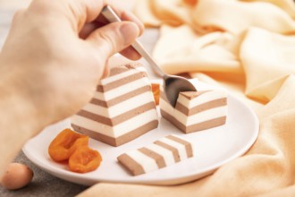 Cocoa and milk jelly with dried apricots with hand on brown concrete background and orange textile,
