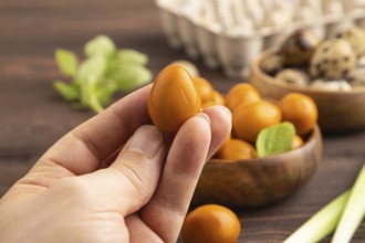 Pile of Smoked Quail eggs in bowl with hand on a brown wooden background. side view, close up,