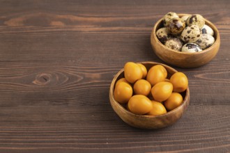Pile of Smoked Quail eggs in bowl on a brown wooden background. side view, copy space