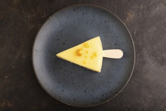 Yellow Cake pop with sprinkles on blue ceramic plate on black concrete background, top view, flat