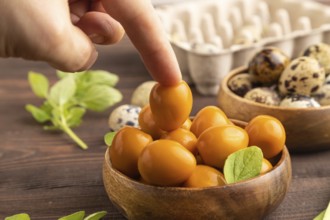 Pile of Smoked Quail eggs in bowl with hand on a brown wooden background. side view, close up,