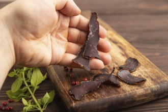 Armenian Basturma dried meat with hand on wooden cutting board with pepper and herbs on brown