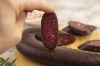 Sujuk sausage with hand on wooden cutting board with pepper and herbs on brown concrete background.