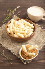 Corn flakes sticks with caramel in wooden bowl on brown wooden background and linen textile. Side