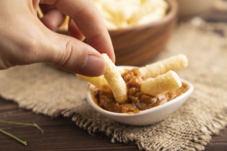 Corn flakes sticks with caramel in wooden bowl with hand on brown wooden background and linen