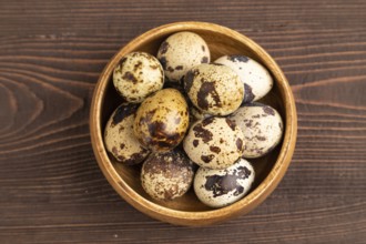 Pile of raw Quail eggs in bowl on a brown wooden background. top view, flat lay, copy space