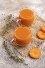 Two glasses with carrot juice, on brown concrete background and linen textile. Diet, healthy eating