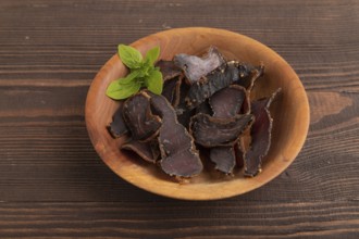 Armenian Basturma dried meat on wooden bowl with pepper and herbs on brown wooden background. Side