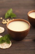 Organic non dairy banana and soy milk in clay cup on brown wooden background. Vegan healthy food