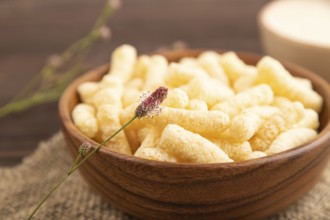 Corn flakes sticks with caramel in wooden bowl on brown wooden background and linen textile. Side