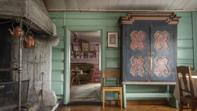 Raum mit großem alten Kamin, einem bemalten Bauernschrank und grüner Holzwand, historischer