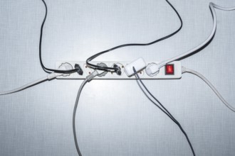 Top view of a power strip with on/off switch and various plugged-in plugs and cables on a white