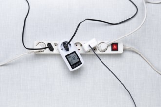 Top view of a power strip with on/off switch and various inserted plugs, cables and an electricity
