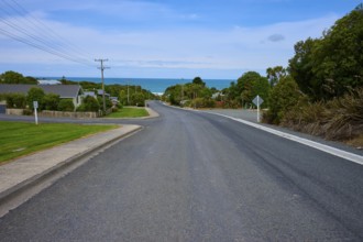 Küstenstraße mit Blick auf das Meer, gesäumt von ruhigen Häusern unter blauem Himmel, Kaka Point,