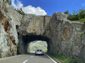 Porsche sports car drives through short rock tunnel Rock tunnel Tunnel on pass road from Alpine