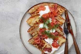 Delicious pancakes with salmon and sour cream, breakfast, on a plate, rustic style, with cutlery