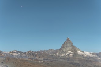 The iconic Matterhorn stands high above a clear evening sky illuminated by a bright moon. This