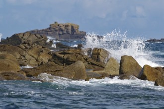 Waves crashing against rocks with a rocky background under a blue sky, Isles of Scilly, Cornwall,